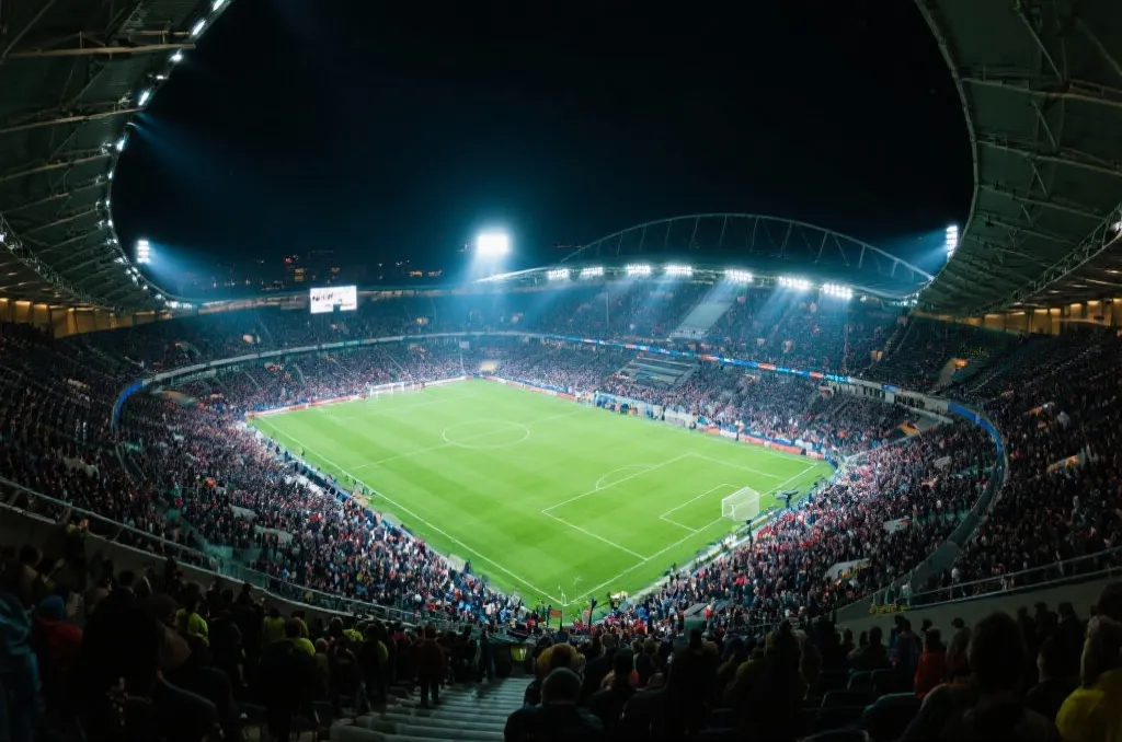 A high-angle view of a modern soccer stadium filled with spectators under bright night lights